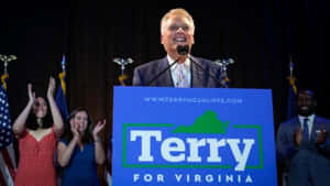 Terry McAuliffe 在維珍尼亞州的競選活動中，與歡呼的支持者和美國國旗一起。