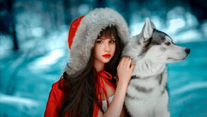 身穿紅色冬季外套的女性在雪地森林中撫摸哈士奇。