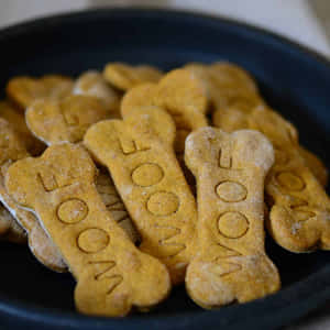 一堆金色骨頭形狀的狗零食，上面壓印著'WOOF'，放在一個深色碗裡。