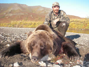 獵人跪在岩石河岸上一隻死去的棕熊旁邊。