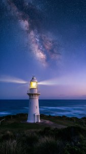 夜晚，燈塔在星空下閃耀，銀河在海洋上空可見。