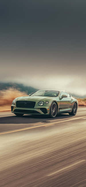 綠色 Bentley 跑車在沙漠公路上奔馳，夕陽西下 — Nothing Phone (3a) Lite 壁紙