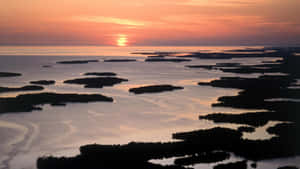 夕陽映照水面，紅樹林島嶼投下深色剪影。 — 日落 壁紙