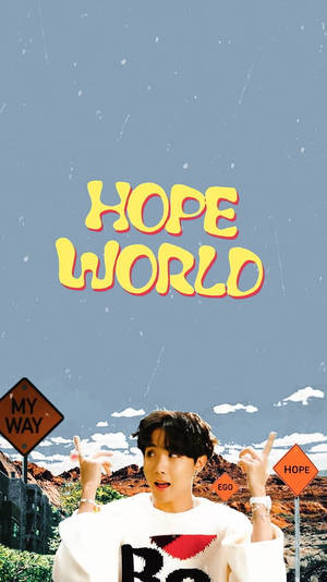 穿著白色毛衣的年輕男子，在沙漠中指向帶有路標的「HOPE WORLD」文字。