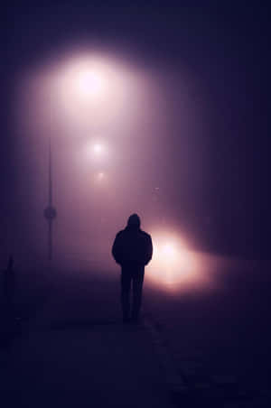 在發光的燈光下，夜間霧氣瀰漫的城市街道上獨自行走的人的剪影。 — 淺紫色動態圖片 壁紙