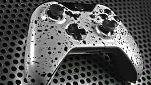 銀色遊戲手掣帶黑色濺漆設計，背景為穿孔金屬。 — Xbox GIF 壁紙