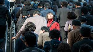 白天通勤時，年輕女子穿著紅色外套站在擁擠的自動扶梯上。