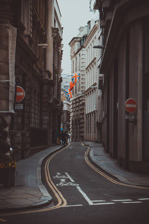 狹窄彎曲的街道，兩旁是歷史悠久的石頭建築，頭頂懸掛著英國國旗。