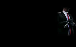 一個穿著西裝和紅色領帶的男人在黑暗中手持槍枝。 — 殺手 壁紙