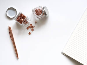 Rose gold stationery items on a white desk surface including push pins and pen.