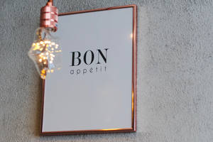 銅框 Bon Appétit 標誌，灰色牆上發光燈泡
