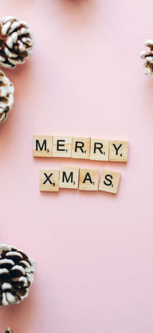 在粉紅色背景上用木製Scrabble字母牌和松果拼出的Merry Xmas。