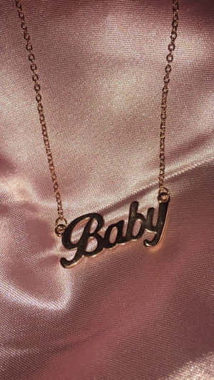 玫瑰金「Baby」吊墜項鍊放在粉紅色緞面布料上。