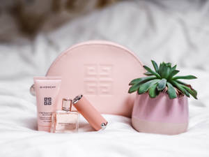 粉紅色 Givenchy 化妝品和多肉植物在白色床上。