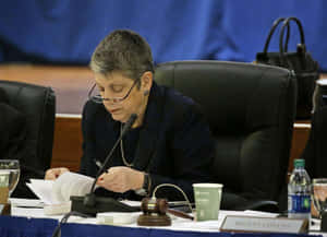 穿著正式服裝的女士在會議桌上閱讀文件，桌上放有木槌。