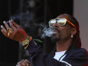Snoop Dogg 戴著金色太陽眼鏡和珠寶呼出煙霧。