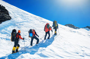 四名登山者穿著鮮豔裝備在藍天下攀登雪山斜坡。