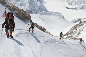 四位登山者用冰斧和繩索攀登雪山斜坡。