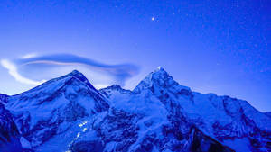 在繁星點點的夜空下，積雪的山脈伴隨著發光的透鏡狀雲。