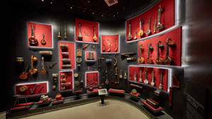 博物館展覽，在紅色燈光牆壁上展示全球樂器。 — 音樂美學 壁紙