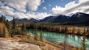 一條綠松石色的河流流經秋日森林，背景是白雪覆蓋的山峰。