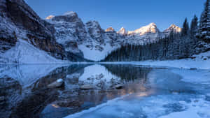 結冰的湖面在日出時分倒映著白雪覆蓋的山脈。