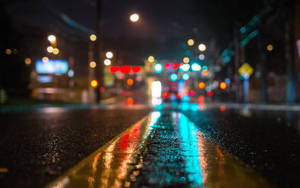 夜雨中的城市街道，模糊的燈光反射在濕漉漉的路面上。