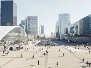 人群在寬敞的城市廣場上漫步，四周環繞著高聳的玻璃和鋼鐵建築。