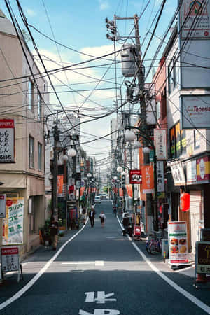 狹窄的日本街道，有商店招牌和架空電線，上方是晴朗的藍天。