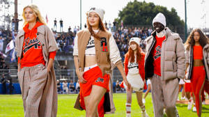 模特兒穿著紅色和米色運動服在時裝秀中走在足球場上。