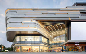 當代曲線白色購物中心，在黃昏時分有明亮的玻璃窗和商店。 — 馬里布 壁紙