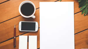 Coffee phone pen paper on wooden desk with green leaves