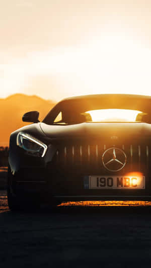黑色 Mercedes-AMG GT 跑車在夕陽下，背景有山脈。