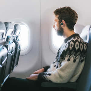 穿圖案毛衣的男士戴著耳機望向飛機窗外
