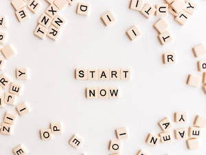 米色字母瓷磚在白色表面上拼出 start now，周圍有散落的字母。