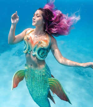 一位粉紅色頭髮、穿著八爪魚上衣的美人魚在水中游泳。