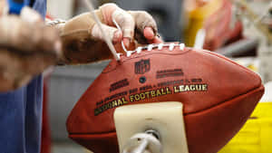 戴手套的手在工場中將鞋帶縫到一個棕色的NFL橄欖球上。