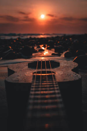 夕陽下潮濕海灘上的烏克麗麗，橙色天空和水面倒影。