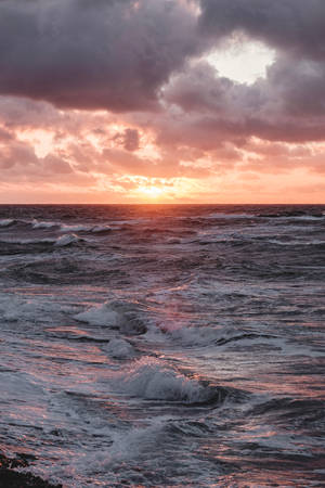 夕陽映照波濤洶湧的海洋，海浪拍打，雲層壯觀。