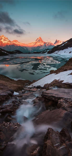 積雪的山峰倒映在冰川湖中，日落時溪流流過岩石。