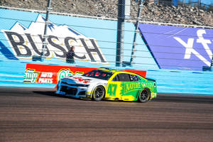 黃綠色NASCAR賽車在賽道上飛馳，背景有廣告。