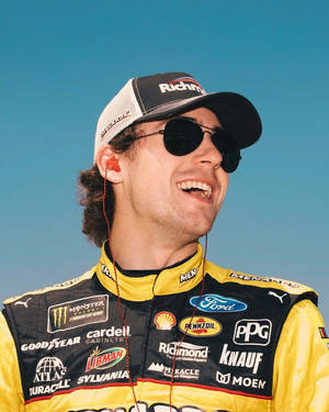 NASCAR車手穿著賽車服微笑，戴著太陽眼鏡和贊助商標誌。