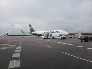 瑞安航空飛機停泊在機場閘口，有地勤人員和服務車輛。
