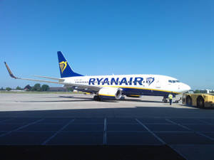 瑞安航空飛機停在機場停機坪，有地勤人員和晴朗藍天。