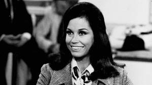 穿著1970年代西裝外套的女性在黑白工作室肖像中微笑。