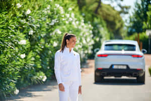 身穿白色運動服的女性走過開花的灌木叢，背景有一輛銀色汽車。