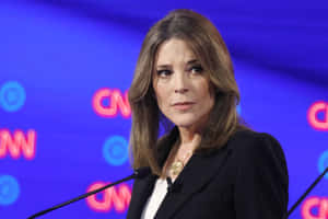 身穿黑色西裝外套的女性在CNN講台上發言，品牌顏色為藍色和粉紅色。