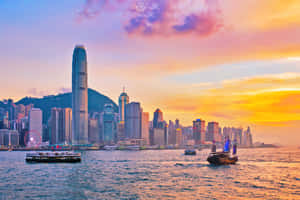 香港日落時分嘅天際線，海港水面有船隻。 — 夜景城市 壁紙