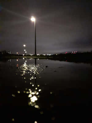 夜晚，路燈在黑暗的天空下倒映在水面上。