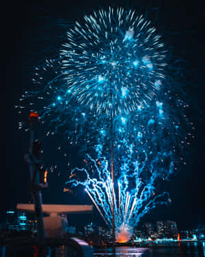 藍色煙火在夜間城市天際線上空綻放，水面有倒影。